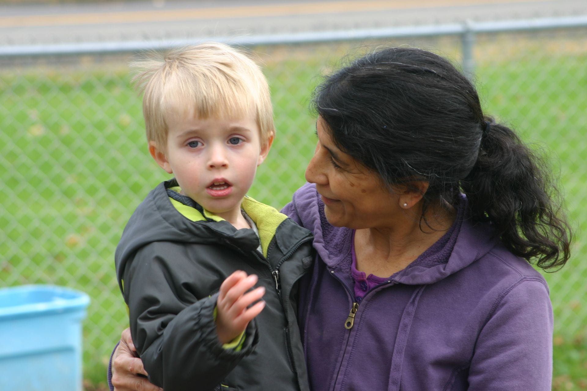 Teacher holds child outside on playground.